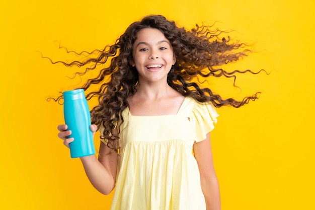 Menina adolescente mostrando condicionadores de xampu de garrafa ou gel de banho isolado em fundo amarelo Produto cosmético para cabelo Mock up frasco Adolescente animado feliz emoções maravilhadas e muito felizes