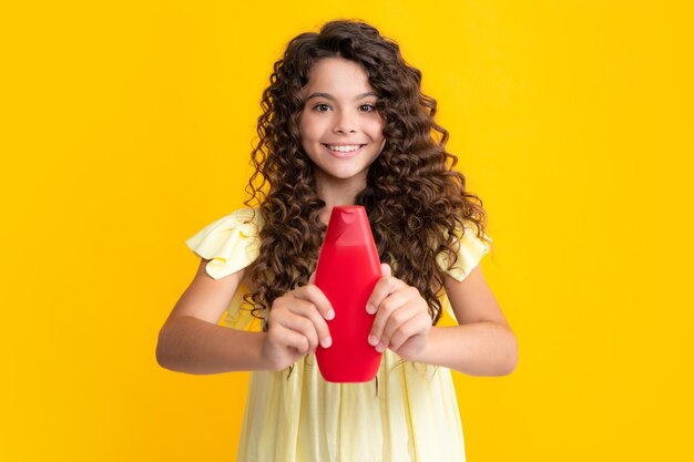 Foto menina adolescente mostrando condicionadores de xampu de garrafa ou gel de banho isolado em fundo amarelo produto cosmético para cabelo mock up garrafa retrato de adolescente feliz menina sorridente