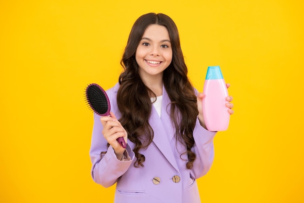 Menina adolescente mostrando condicionadores de xampu de garrafa ou gel de banho isolado em fundo amarelo Produto cosmético para cabelo Mock up garrafa Rosto feliz emoções positivas e sorridentes de adolescente