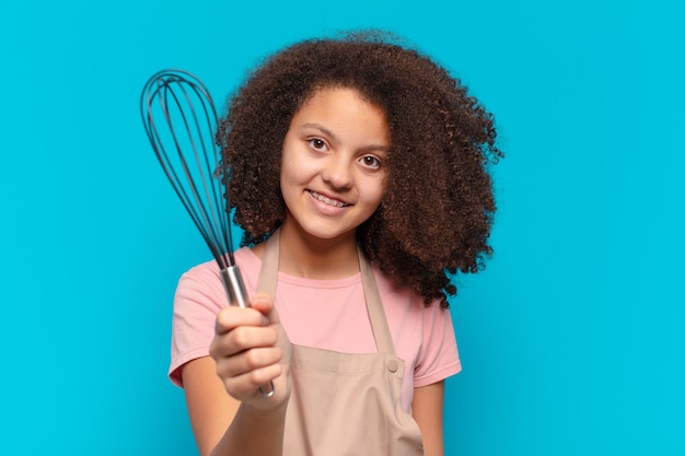 Menina adolescente muito afro cozinhando com um avental e uma batedeira. conceito de padeiro