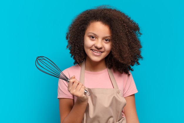 Menina adolescente muito afro cozinhando com um avental e uma batedeira. conceito de padeiro