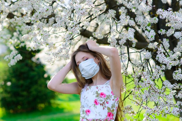 Menina adolescente na máscara médica no jardim florido de primavera. Conceito de distância social e prevenção do coronavírus.