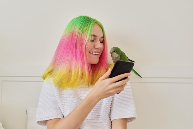 Foto menina adolescente na moda com smartphone e papagaio quaker verde jovem no ombro, em casa na cama. proprietário do animal de estimação falando em comunicação de vídeo, amizade de pássaros humanos, estilo de vida, comunicação
