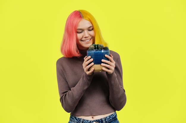 Menina adolescente na moda sorridente com cacto em vaso em fundo amarelo Conceito de estilo de vida de psicologia da adolescência da juventude