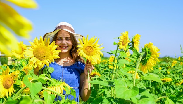 Menina adolescente no conceito de campo de girassol de férias de verão rica colheita e agricultura criança de infância feliz usa chapéu de palha de verão criança no campo de flores amarelas cheio de alegria