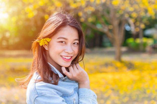 Menina adolescente nova asiática bonita com outono da flor do amarelo da natureza.