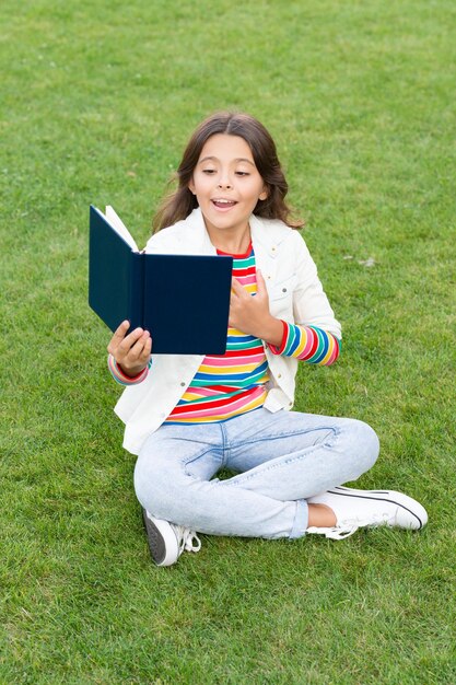 Menina adolescente orgulhosa lê livro sentado na grama lendo livro menina leitora com livro ao ar livre