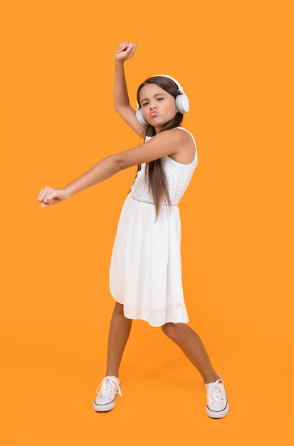 Foto menina adolescente ouve música em fones de ouvido e dança em fundo amarelo