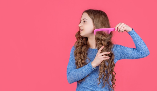 Menina adolescente penteando cabelos cacheados com escova de cabelo em fundo rosa com espaço de cópia