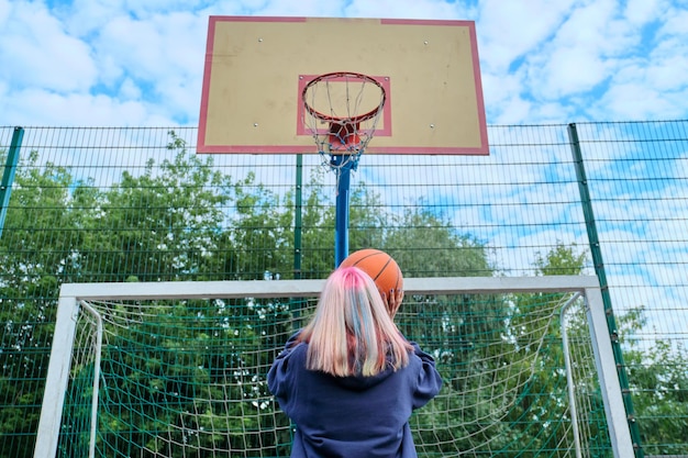 Menina adolescente pulando com bola jogando basquete de rua, vista traseira. estilo de vida saudável ativo, hobbies e lazer, conceito de juventude