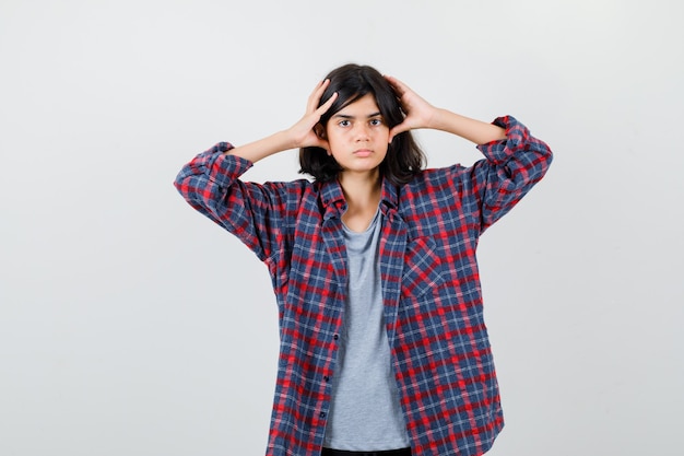 Menina adolescente segurando a cabeça com os dedos na camisa quadriculada e parecendo cansada, vista frontal.