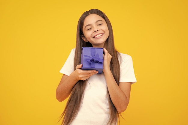 Menina adolescente segurando a caixa de presente isolada em fundo amarelo Presente para aniversário de crianças