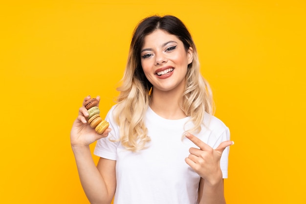 Menina adolescente segurando macarons franceses coloridos e apontando-os