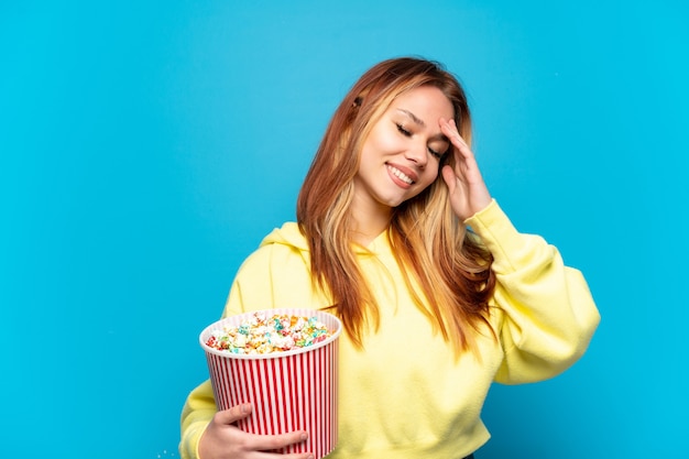 Menina adolescente segurando pipocas sobre um fundo azul isolado e sorrindo muito