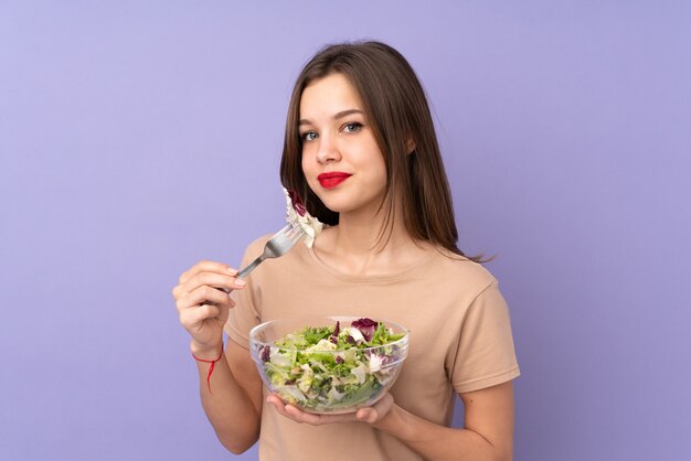 Menina adolescente segurando salada isolada na parede roxa