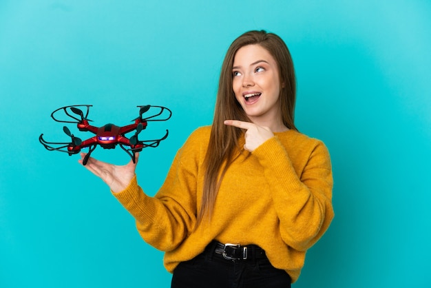 Menina adolescente segurando um drone sobre um fundo azul isolado com a intenção de perceber a solução enquanto levanta um dedo