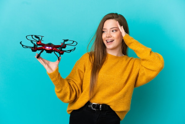 Menina adolescente segurando um drone sobre um fundo azul isolado e sorrindo muito