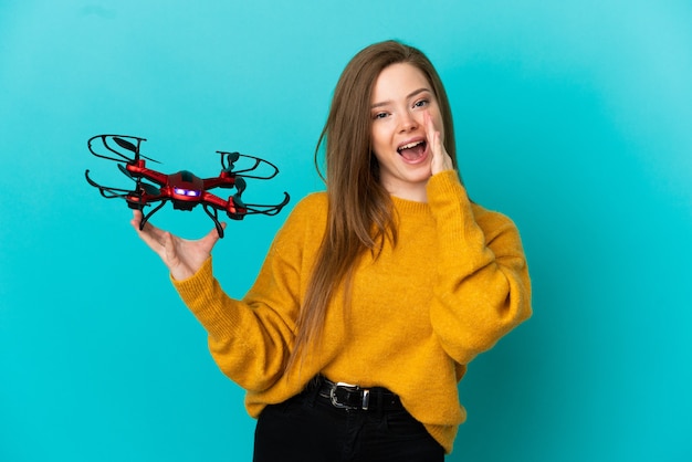 Menina adolescente segurando um drone sobre um fundo azul isolado, gritando com a boca bem aberta