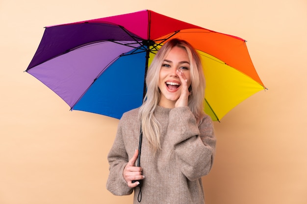 Menina adolescente segurando um guarda-chuva sobre parede isolada, gritando com a boca aberta