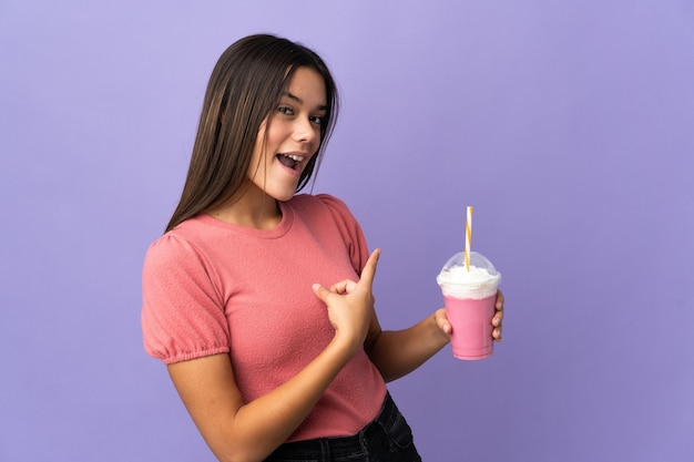 Menina adolescente segurando um milkshake de morango apontando para trás