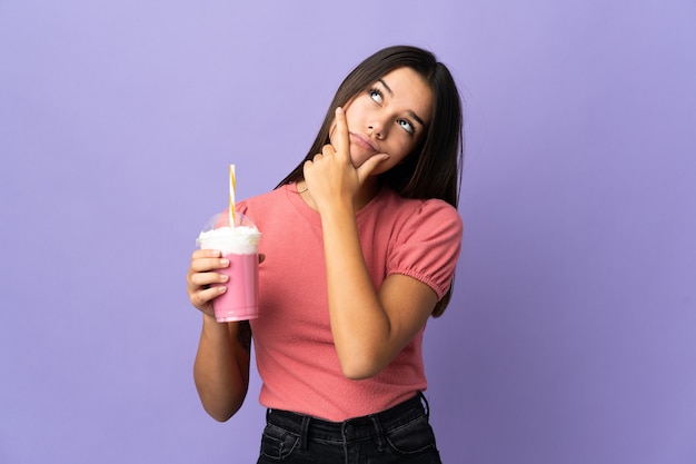 Menina adolescente segurando um milkshake de morango e tendo dúvidas