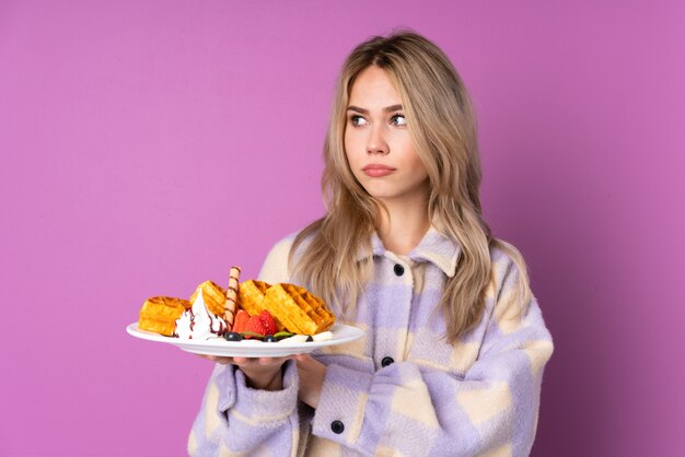 Menina adolescente segurando waffles isolados no retrato roxo