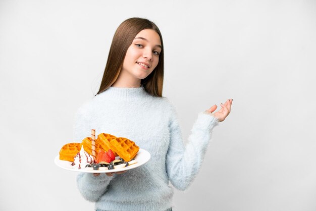 Menina adolescente segurando waffles sobre fundo branco isolado, estendendo as mãos para o lado para convidar para vir