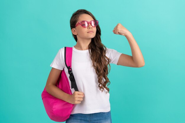 Menina adolescente séria carrega mochila de volta ao conceito de dia de conhecimento escolar de educação criança em óculos de sol em fundo azul 1 de setembro criança de infância com bolsa de escola mostra seu poder