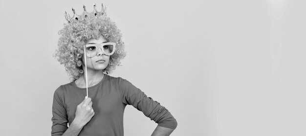 Menina adolescente séria em peruca de palhaço extravagante usa coroa de rainha e óculos de festa engraçados arrogante Criança adolescente engraçada em cartaz de festa de peruca Espaço de cópia de cabeçalho de banner