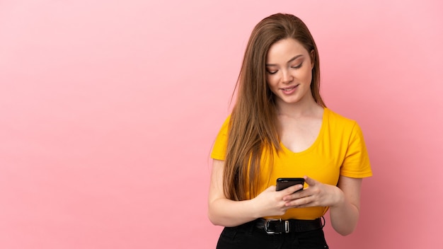 Menina adolescente sobre fundo rosa isolado enviando uma mensagem com o celular