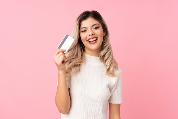 Foto menina adolescente sobre fundo rosa isolado, segurando um cartão de crédito