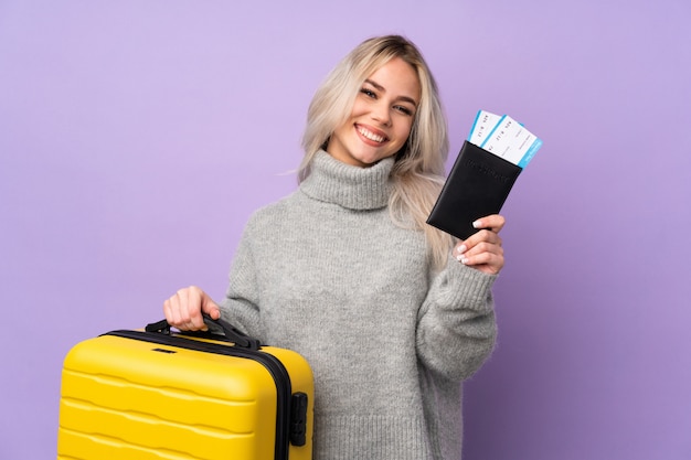 Menina adolescente sobre fundo roxo isolado em férias com mala e passaporte