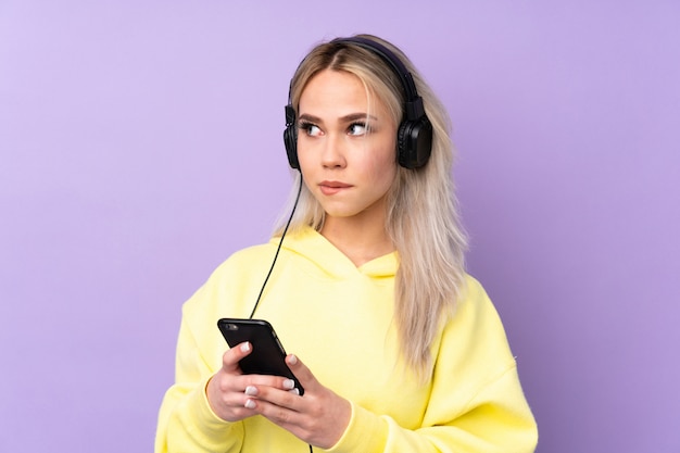 Menina adolescente sobre música de fundo roxo isolado, com um celular e pensamento