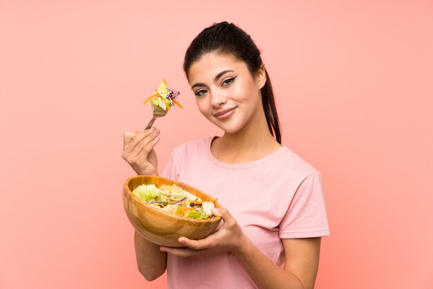 Menina adolescente sobre parede rosa isolada com salada