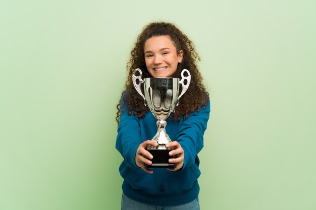 Menina adolescente sobre parede verde segurando um troféu