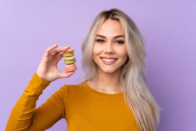 Menina adolescente sobre roxo isolado segurando macarons franceses coloridos