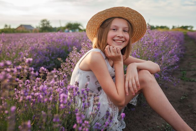 Menina adolescente sonhadora com chapéu de palha sentada no campo de lavanda, beleza da natureza, estilo de vida de verão