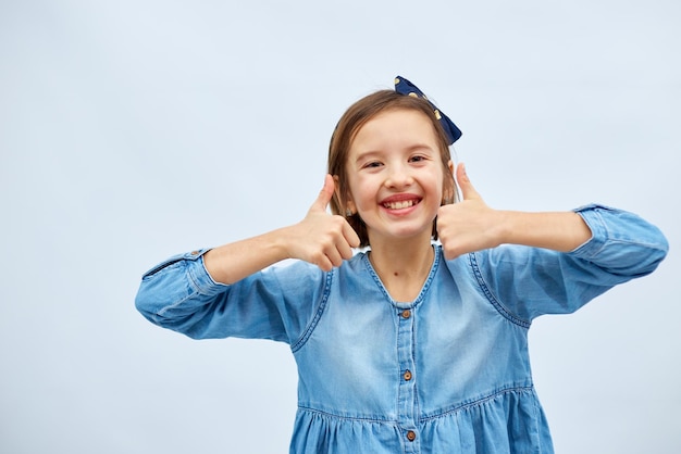 Menina adolescente sorridente em vestido jeans compõe o polegar para cima