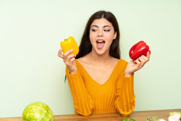 Menina adolescente surpreendida com muitos legumes sobre parede verde