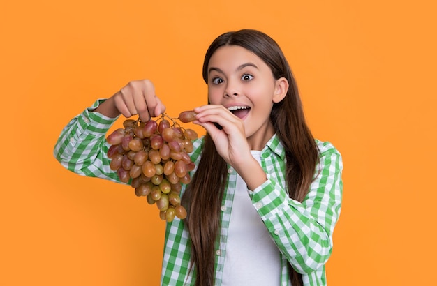 Foto menina adolescente surpreendida com um feixe de uvas em fundo amarelo