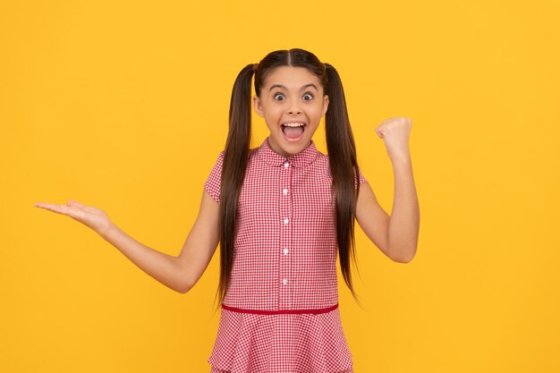 Menina adolescente surpresa que apresenta o produto no espaço de cópia de fundo amarelo celebra a promoção do sucesso