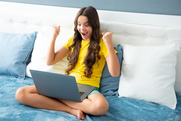 Menina adolescente trabalhando no computador portátil pc deitada na cama descansando relaxando no quarto em casa menina adolescente Expressiva emocional excitada adolescente