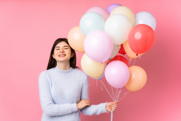 Menina adolescente ucraniana segurando muitos balões sobre parede rosa isolada rindo