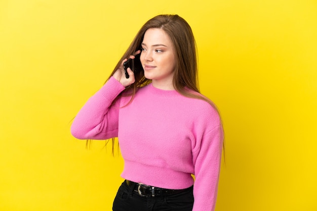 Menina adolescente usando telefone celular sobre fundo amarelo isolado, olhando de lado