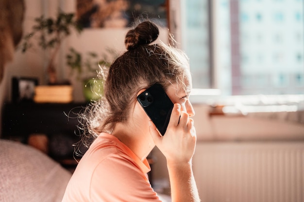 Menina adolescente verificando as mídias sociais segurando o smartphone em casa Jovem sorridente usando o aplicativo para celular jogando compras on-line