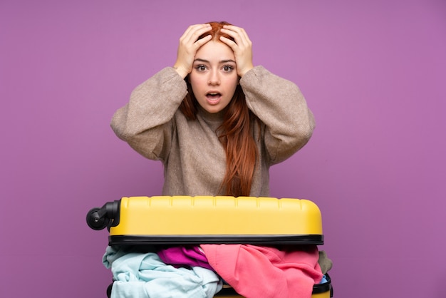 Menina adolescente viajante com uma mala cheia de roupas com expressão facial de surpresa