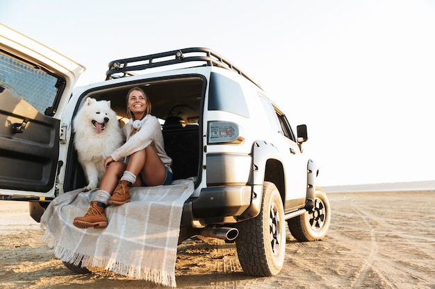 Menina adorável alegre brincando com seu cachorro enquanto está sentada em um carro na praia