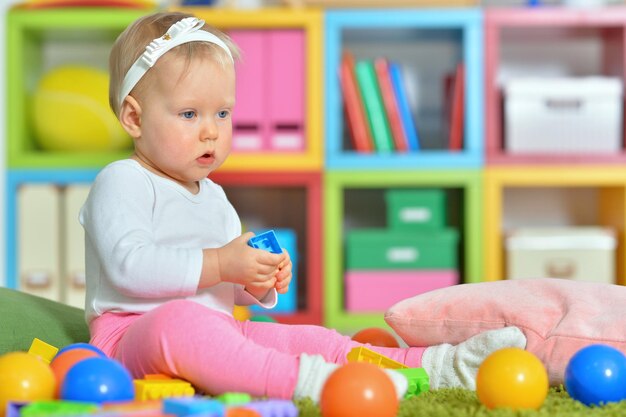 Menina adorável brincando com brinquedos coloridos na sala de jogos