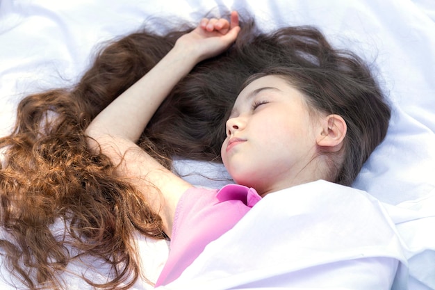 Foto menina adorável com cabelos extra longos deitada em lençóis brancos dormindo debaixo de cobertor