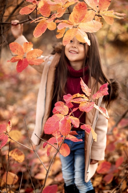 Menina adorável feliz brincando com folhas de outono. foco nas folhas